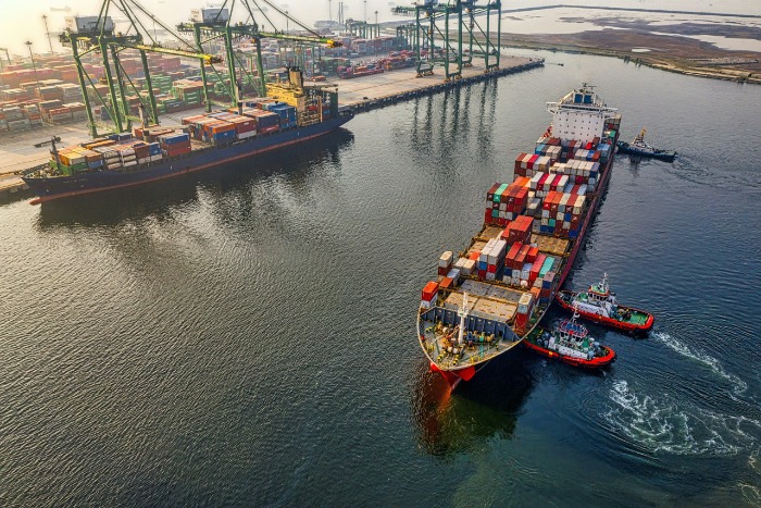 Vista aérea de un buque portacontenedores navegando cerca de grúas en un puerto marítimo de carga para la agroexportación.