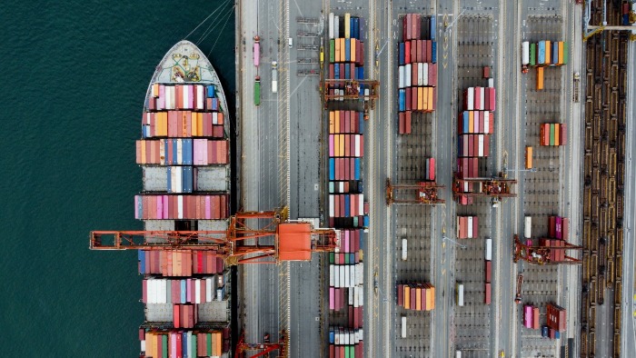 Vista aérea de un buque portacontenedores amarrado en un puerto comercial descargando contenedores refrigerados para la exportación marítima. 