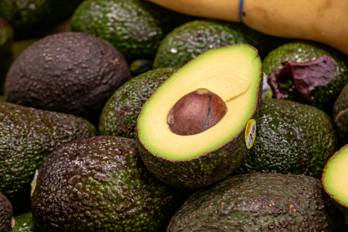 Aguacates frescos cortados a la mitad sobre una pila de fruta en un mercado mayorista. 