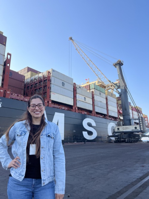 Sara Lynn Álvarez sonriendo frente a un buque portacontenedores de MSC en la terminal portuaria de Pisco. 